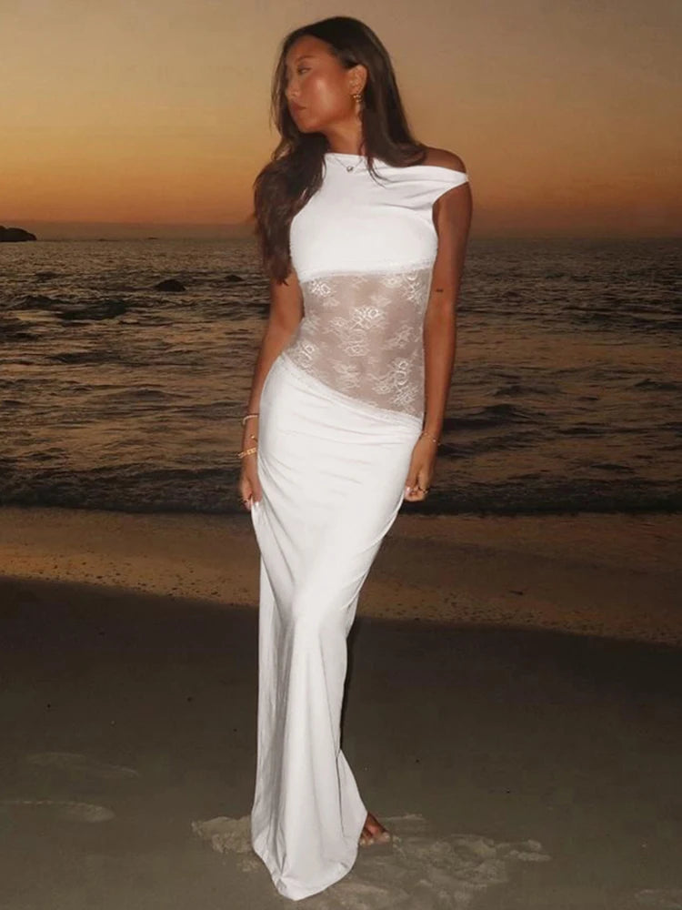 Mulher usando versão branca do vestido Obsession, com renda lateral, posando ao entardecer na praia.