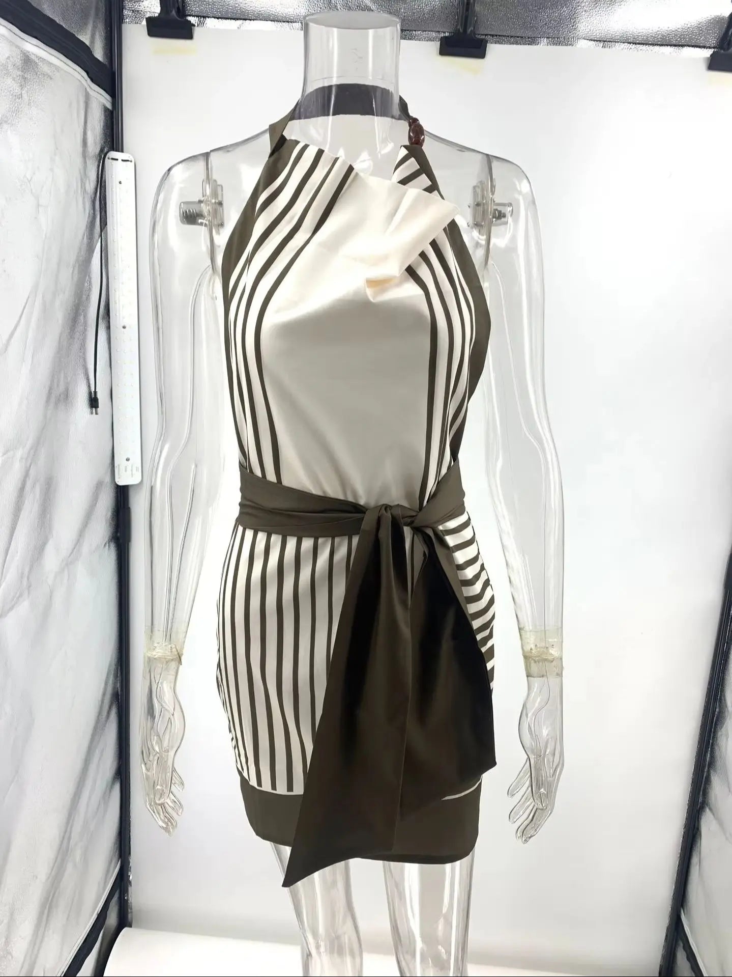Vestido Rubi curto sobre manequim branco, mostrando estampa assimétrica e faixa lateral em verde-militar