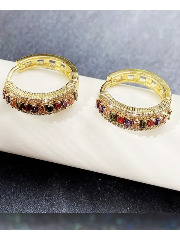 Brinco Valentina dourado com zircônias coloridas apoiado sobre tecido claro, visual sofisticado e elegante.