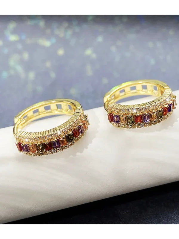 Brinco Valentina dourado com zircônias coloridas apoiado sobre superfície clara, estilo moderno e refinado.