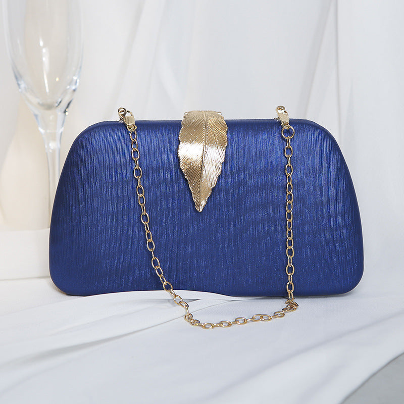 Clutch azul sofisticada com detalhe de folha dourada e corrente delicada, perfeita para casamentos.