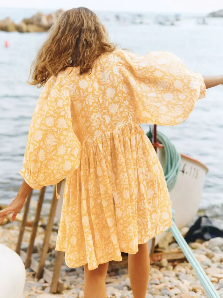 Vista traseira do vestido floral amarelo com movimento leve, ideal para usar na praia ou em viagens tropicais.