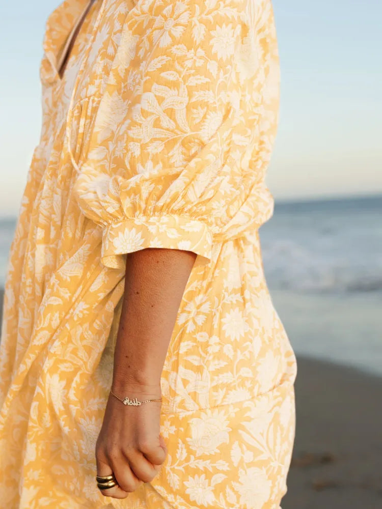 Detalhe da manga bufante e da estampa floral do vestido curto amarelo com tecido leve, em look de verão à beira-mar.