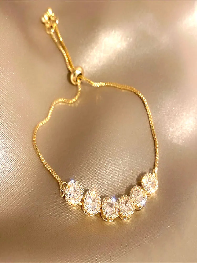 Close da Pulseira Luxor sobre tecido acetinado claro, exibindo detalhes dos cristais lapidados e banho dourado