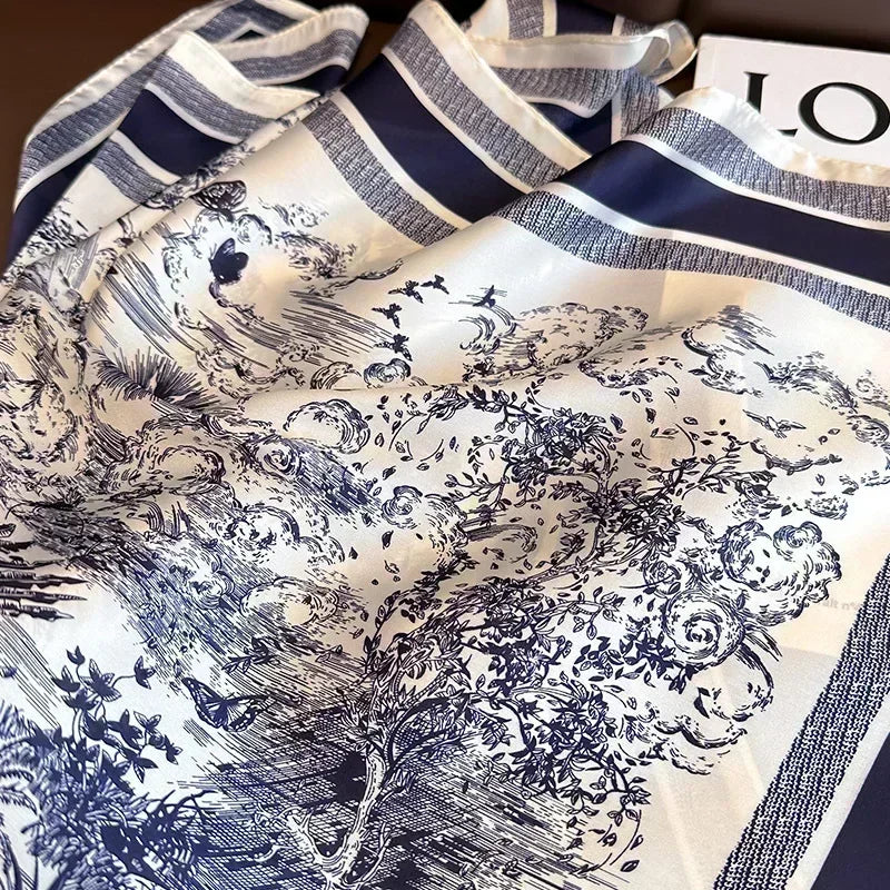 Dois lencos Versatile Grace com estampa toile de jouy azul dispostos lado a lado sobre banco marrom