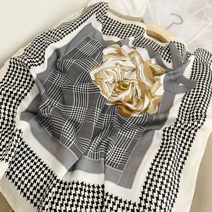 Lenco Versatile Grace com padronagem xadrez preta e branca, flor dourada central e moldura em tons de cinza claro