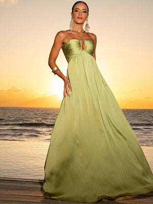 Modelo usando o Vestido Eden Verde Plissado com decote halter, vista frontal ao pôr do sol à beira-mar.


