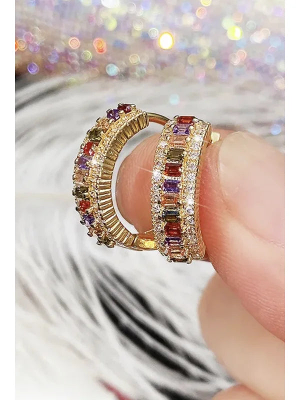 Brinco Valentina dourado com zircônias coloridas sendo segurado na mão, detalhe de lapidação e brilho intenso.
