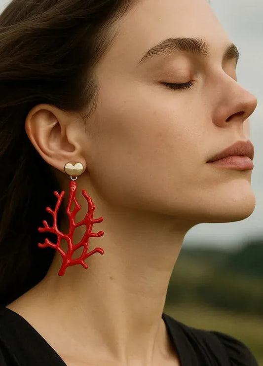 Brincos Coralina em formato de coral vermelho com detalhe dourado em coração, usados por modelo em look elegante.