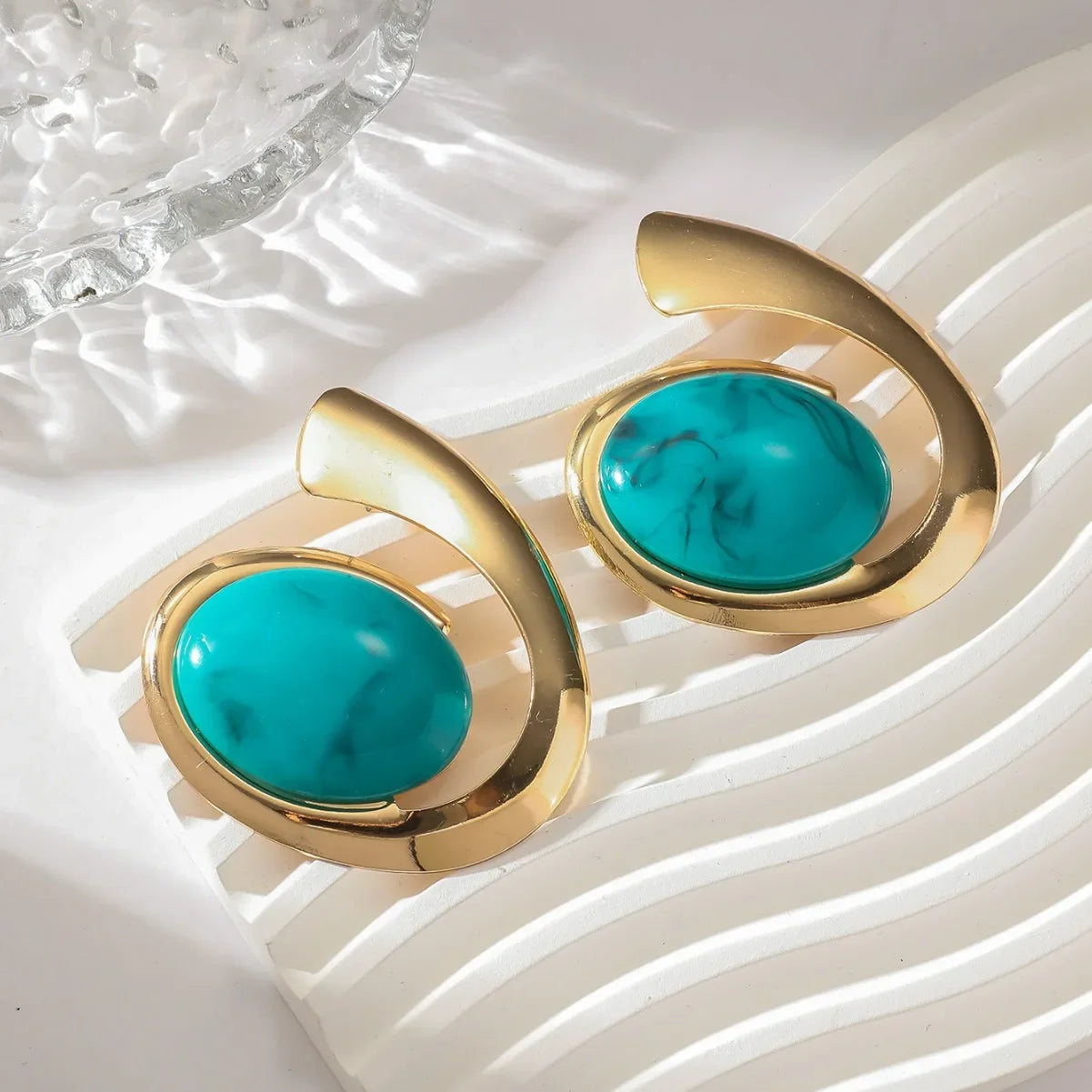 Par de brincos espiral dourado com pedra azul, fundo claro minimalista