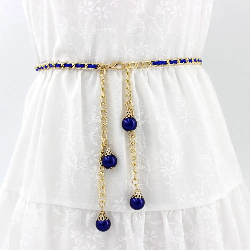 Cinto Aurora azul marinho com acabamento em corrente dourada e esferas decorativas, realçando looks sofisticados.