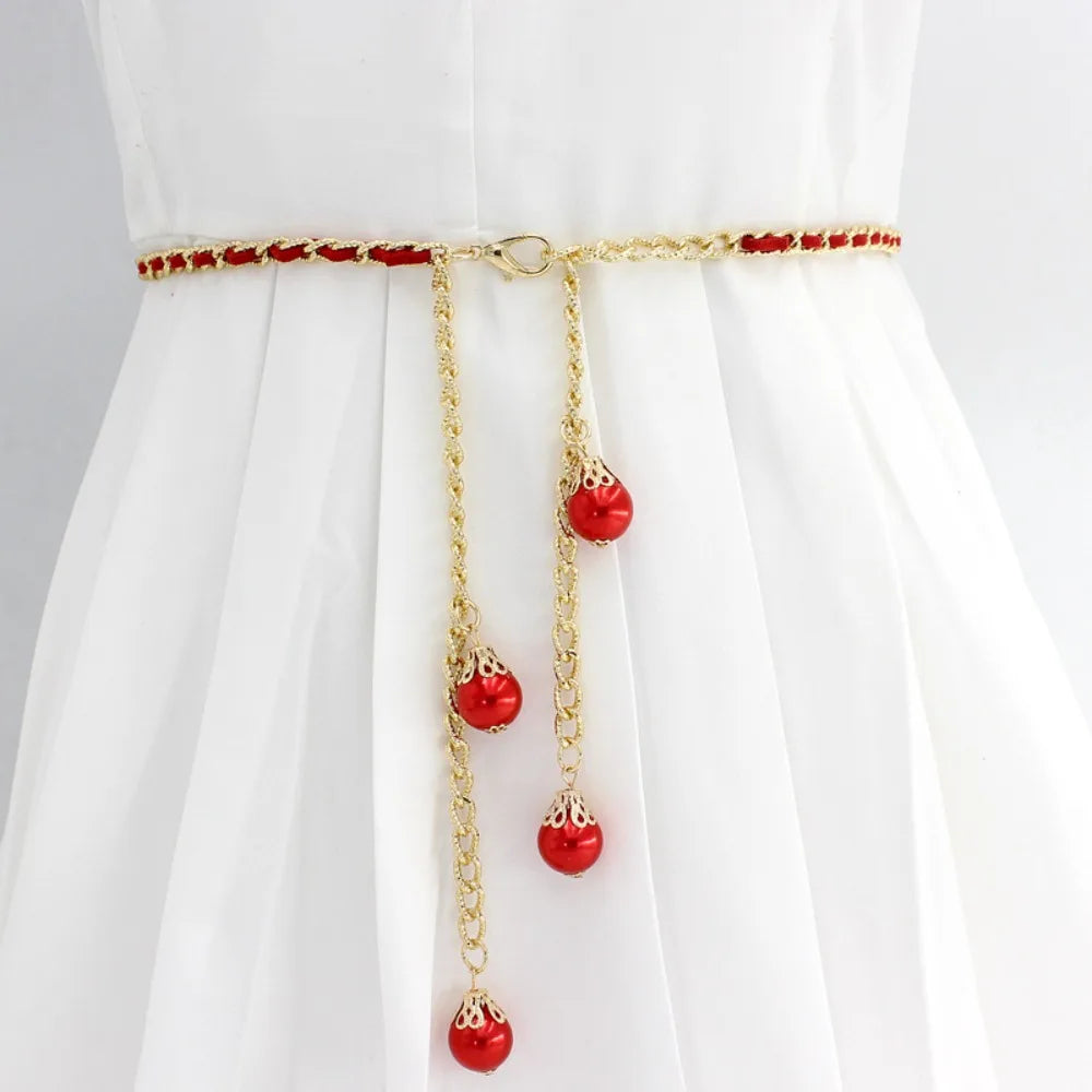 Cinto Aurora vermelho com corrente dourada e esferas decorativas, ideal para adicionar cor ao visual.

