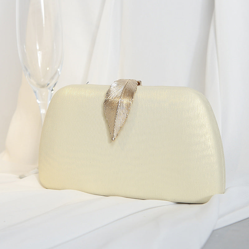 Clutch bege estruturada com detalhe de folha dourada, opção versátil para produções elegantes.