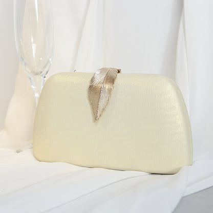 Clutch bege estruturada com detalhe de folha dourada, opção versátil para produções elegantes.