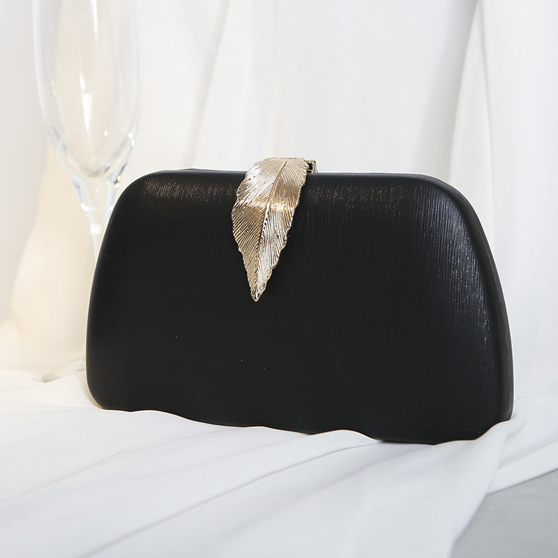 Clutch preta rígida com detalhe de folha dourada, combinação clássica para eventos noturnos.