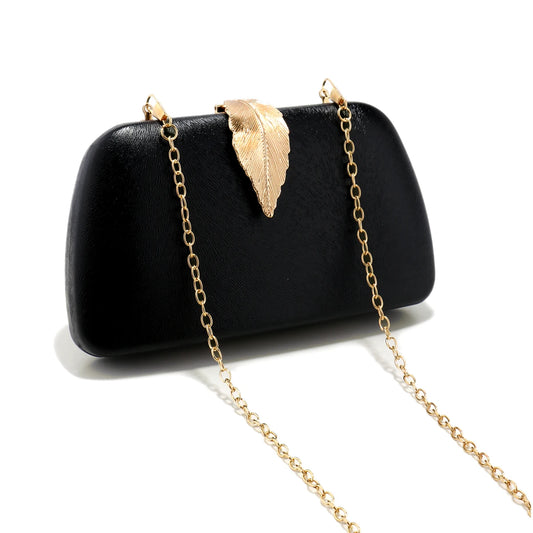 Clutch preta estruturada com detalhe de folha dourada e alça em corrente, ideal para festas sofisticadas.