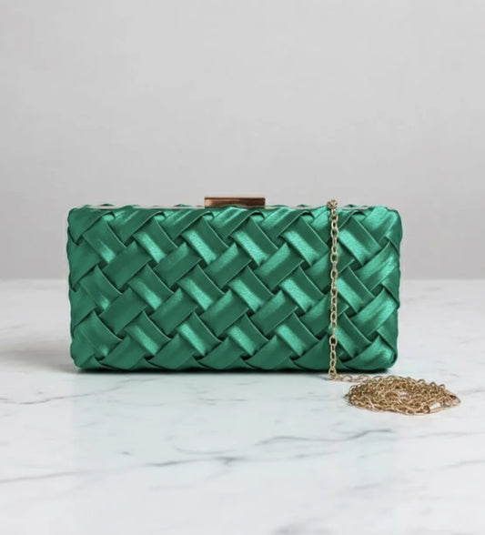 Clutch verde elegante Dress Eleven com textura trançada em cetim e corrente dourada sobre superfície marmorizada.