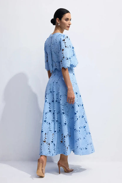 Modelo de perfil com o Conjunto Antonella de renda floral azul claro, mostrando o caimento elegante da saia e o detalhe das mangas amplas da blusa cropped em estúdio.