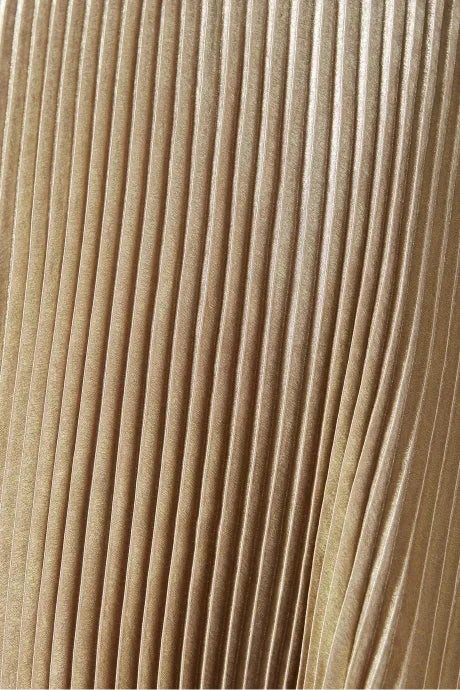Close do tecido plissado dourado com acabamento acetinado do Vestido Vênus da Dress Eleven, evidenciando o brilho e a textura do material

