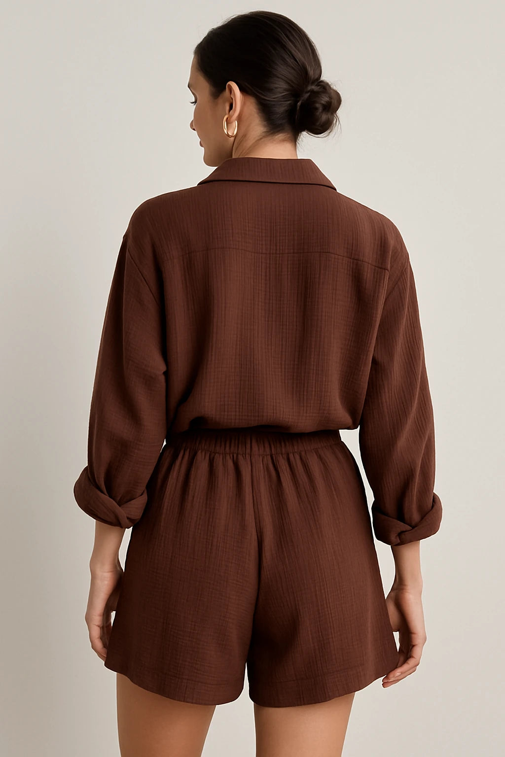 Vista traseira do conjunto marrom com camisa ampla e shorts de cintura alta, cabelo preso em coque elegante.