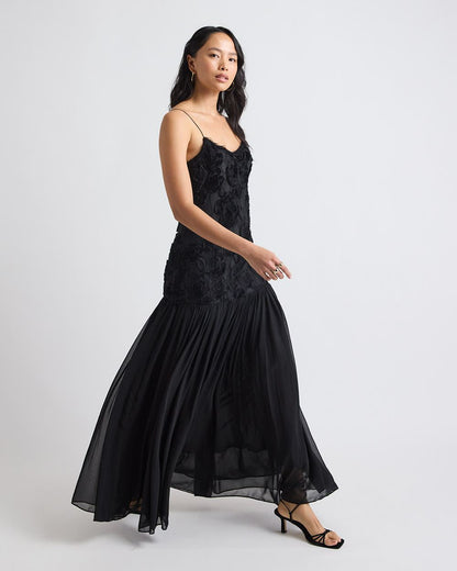 Vestido Ágata longo preto em movimento, com saia plissada fluida e busto bordado em flores 3D.