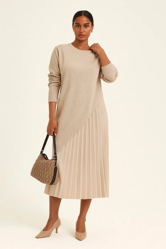Mulher morena clara vestindo vestido bege com sobreposição assimétrica e saia plissada em estúdio claro. Look elegante e sofisticado da Dress Eleven.