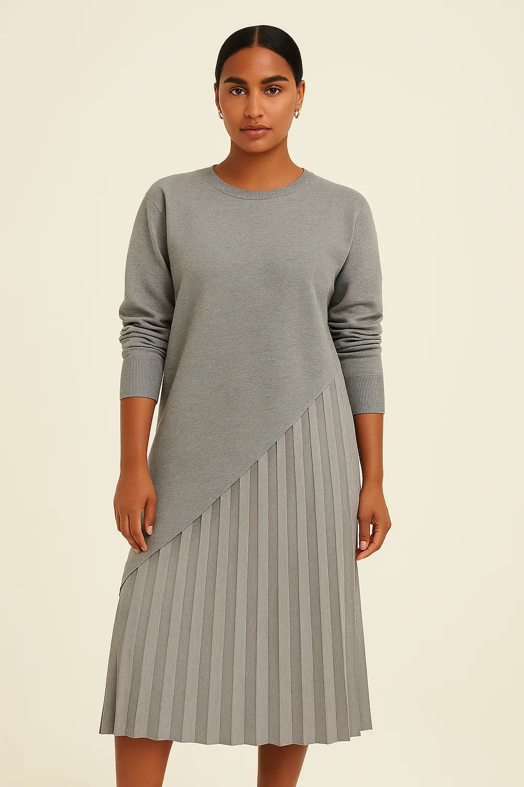  Modelo morena clara com vestido cinza assimétrico e saia plissada no estúdio da Dress Eleven. Sofisticação atemporal com toque minimalista.