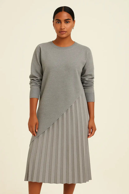  Modelo morena clara com vestido cinza assimétrico e saia plissada no estúdio da Dress Eleven. Sofisticação atemporal com toque minimalista.