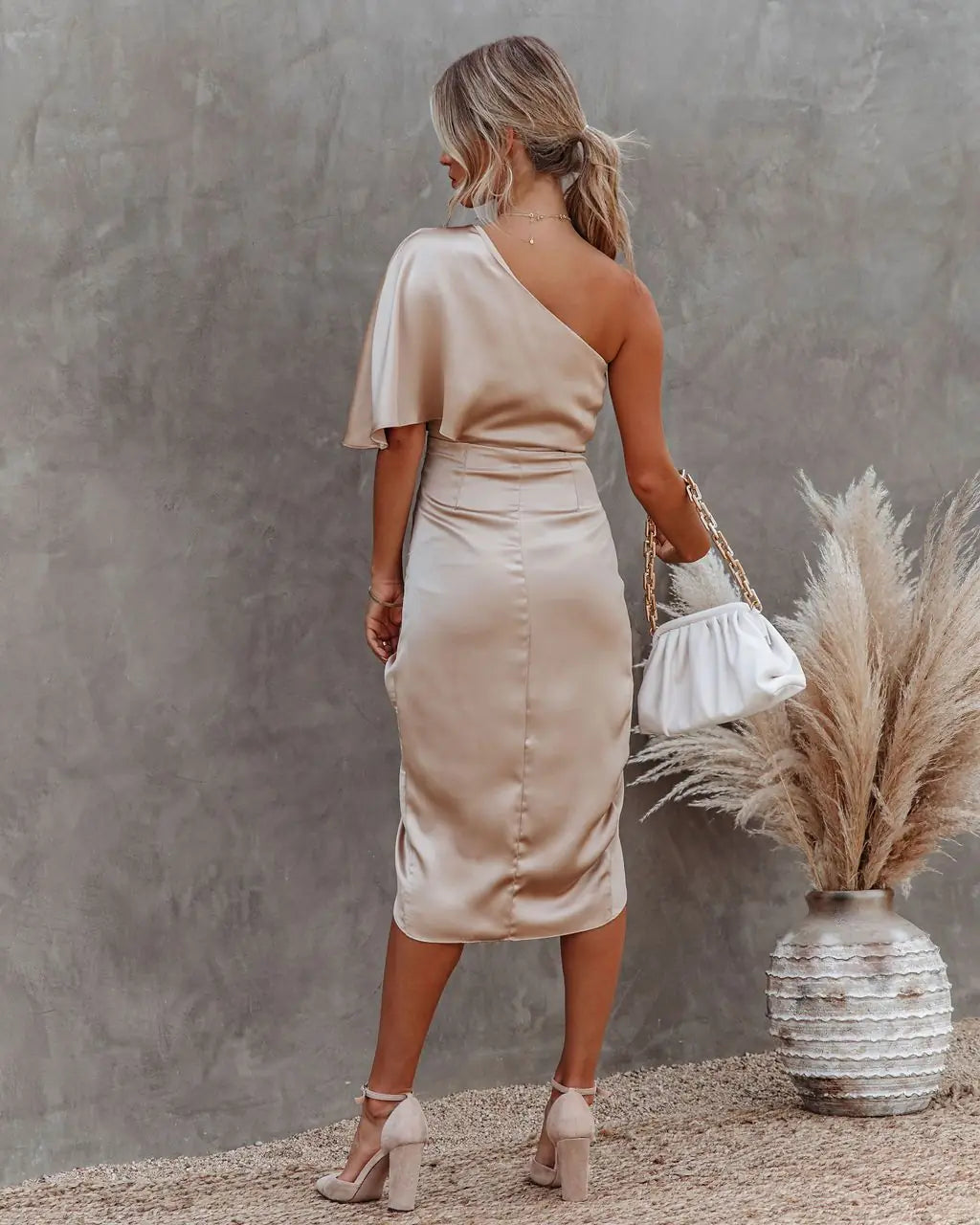 Vestido Athena midi bege visto de costas, cintura marcada e detalhe assimétrico.