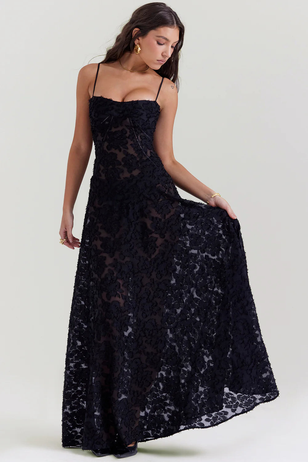 Vestido longo Blair preto em poliéster bordado, modelo segurando a saia para destacar o caimento fluido.
