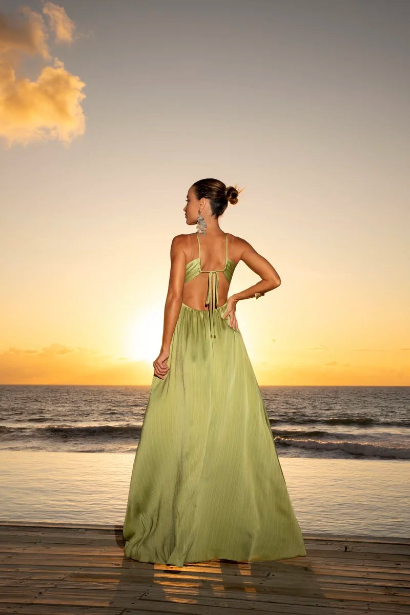 Vestido Eden Halter verde com decote halter e amarração nas costas, saia plissada longa em cenário de pôr do sol