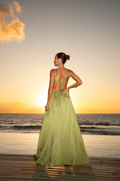 Vestido Eden Halter verde com decote halter e amarração nas costas, saia plissada longa em cenário de pôr do sol