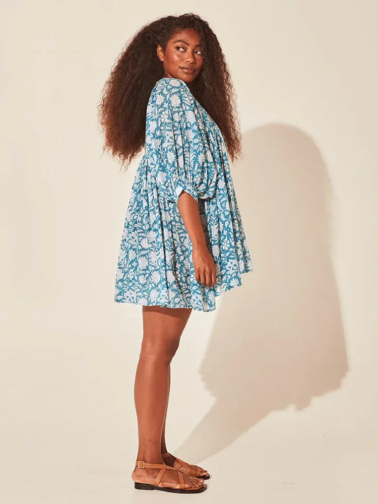 Vista lateral do vestido floral azul com modelagem soltinha, em estúdio com iluminação que destaca o volume da peça.