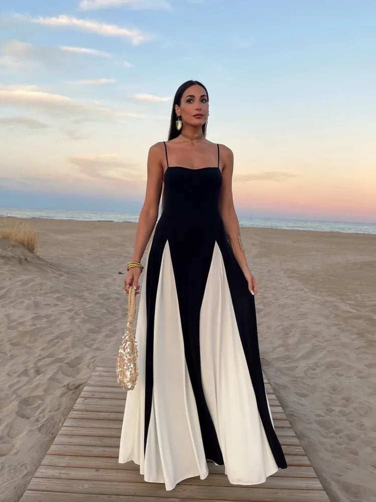 Mulher usando vestido longo bicolor preto e branco Adele ao pôr do sol na praia, com alças finas e caimento fluido.