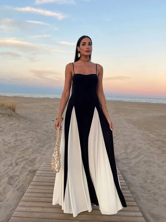 Mulher usando vestido longo bicolor preto e branco Adele ao pôr do sol na praia, com alças finas e caimento fluido.