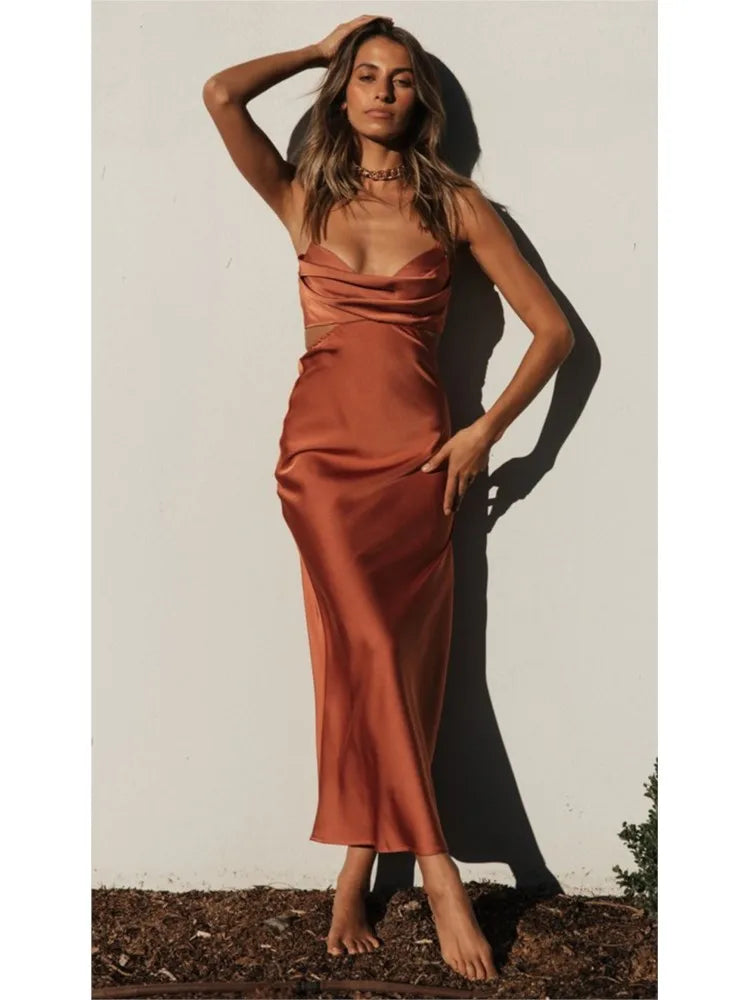 Vestido de cetim terracota com decote drapeado e alças finas, fotografado sob luz do sol com estilo sensual e elegante.

