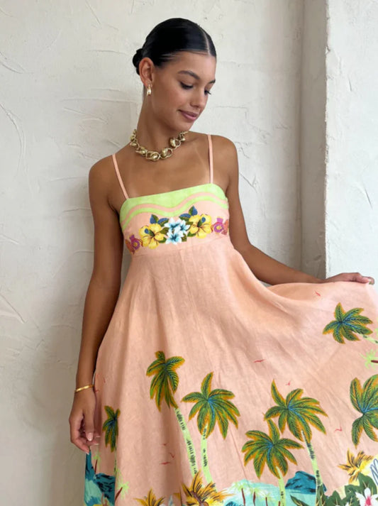 Vestido midi tropical com estampa praiana e fundo claro, modelo segurando a saia para destacar o caimento fluido.