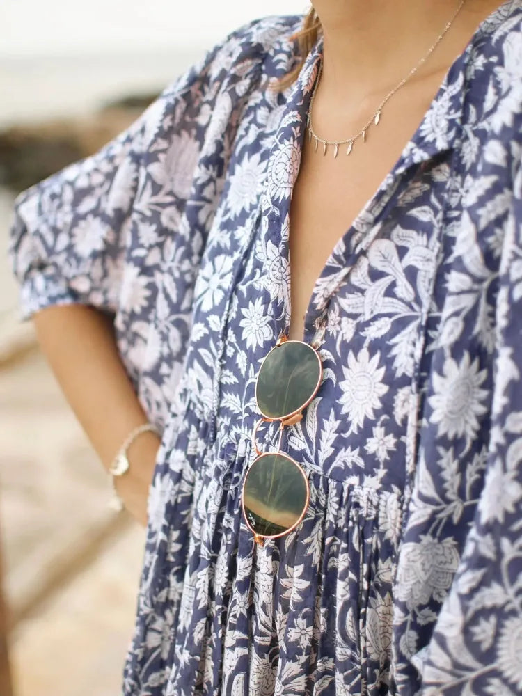 Detalhe do decote em V e estampa floral do Vestido Oceana, com óculos de sol pendurado