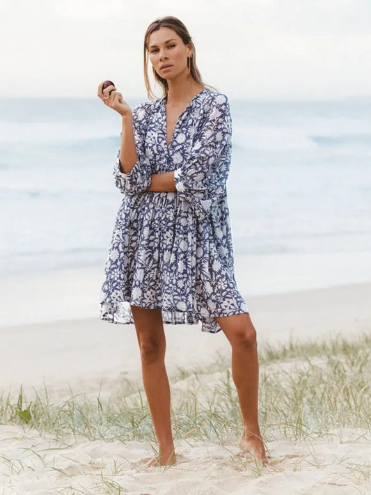 Modelo usando o Vestido Oceana floral azul marinho, com mangas amplas e shape soltinho, em cenário de praia