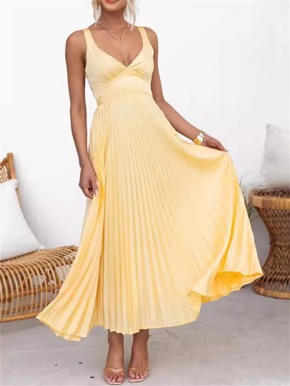 Vestido Solaré em cetim amarelo em movimento, destacando a fluidez da saia plissada e o charme das alças delicadas.