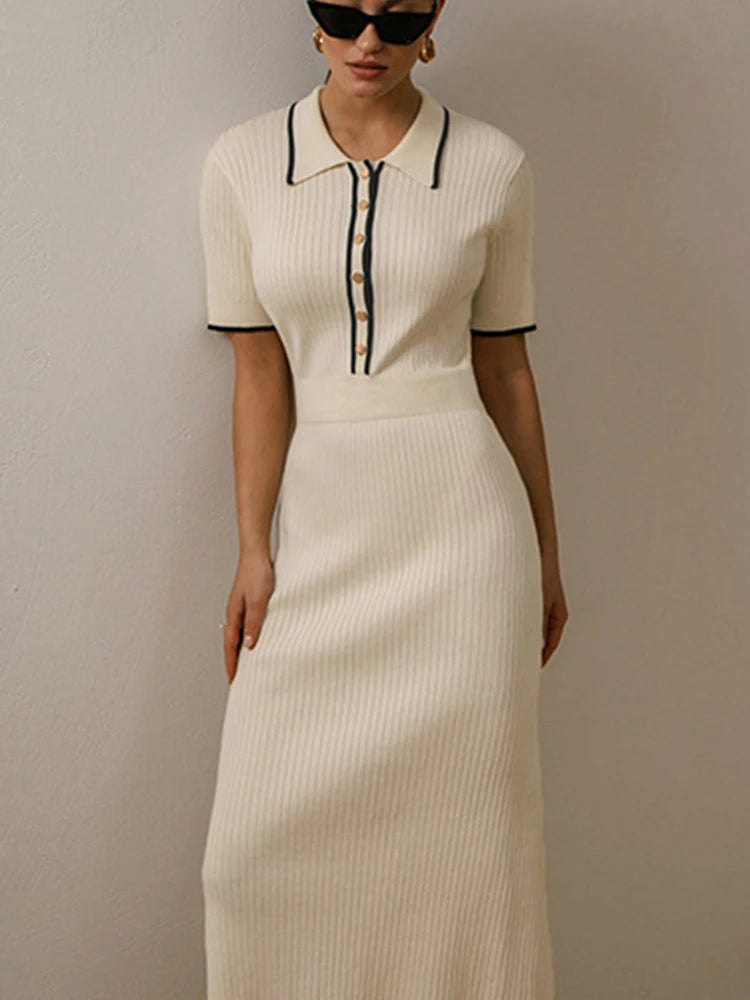 Vestido em tricot off-white com gola polo e botões dourados, modelo em pé com fundo claro.

