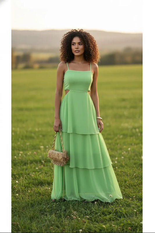 Vestido Babi verde Dress Eleven em chiffon fluido, com alças finas, recorte na cintura e babados elegantes, fotografado em campo ao pôr do sol.