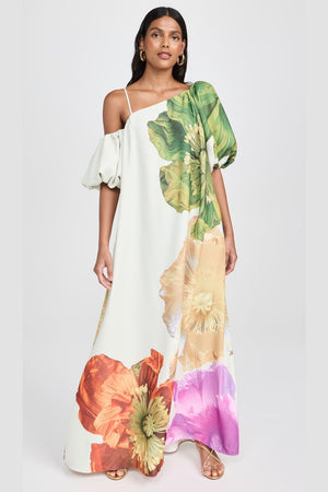 Vestido Hera floral longo com estampa artística e modelagem ombro único, usado por modelo em pé com sandálias douradas.