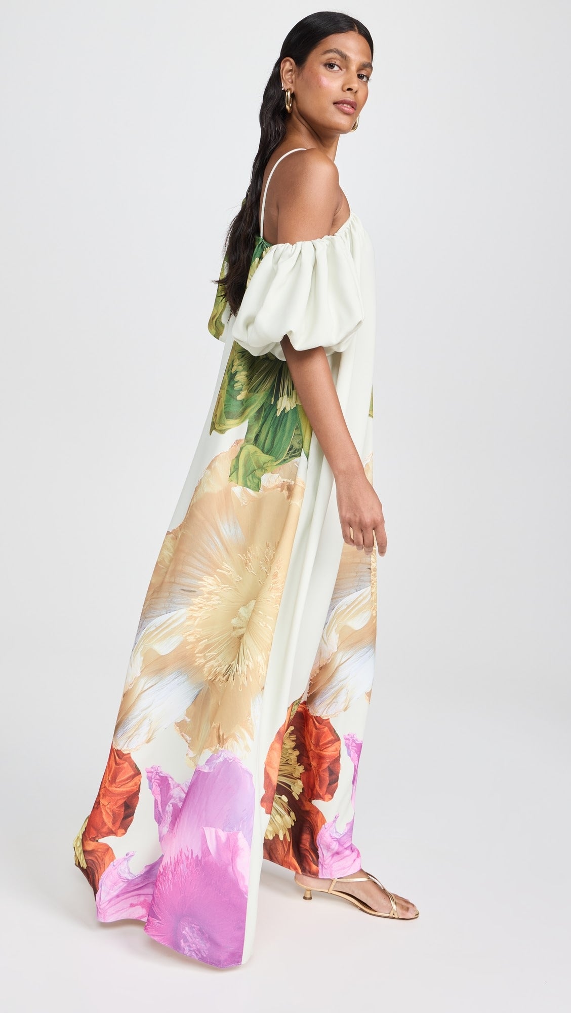 Modelo em pose diagonal usando o vestido Hera floral com ombro único e estampa vibrante em tons de verde, rosa e laranja.

